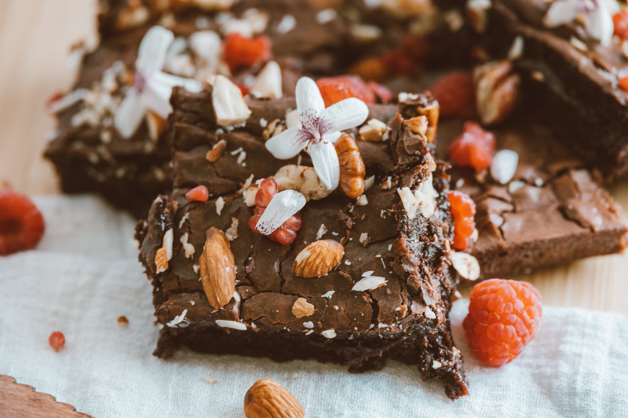 Close-up of homemade brownies topped with almonds and raspberries, highlighting floral decorations for an artistic touch.